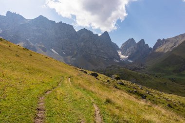 Gürcistan, Kazbegi Bölgesi 'ndeki Büyük Kafkasya Dağları' ndaki Chaukhi topluluğunun keskin dağ zirvelerine panoramik bir manzara. Yeşil bir çayırda yürüyüş parkuru. Gürcü Dolomitler.