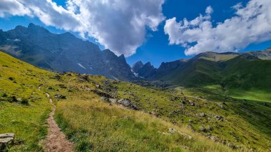 Gürcistan, Kazbegi Bölgesi 'ndeki Büyük Kafkasya Dağları' ndaki Chaukhi topluluğunun keskin dağ zirvelerine panoramik bir manzara. Yeşil bir çayırda yürüyüş parkuru. Gürcü Dolomitler.