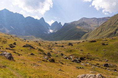 A panoramic view on the sharp mountain peaks of the Chaukhi massif in the Greater Caucasus Mountain Range in Georgia, Kazbegi Region. A hiking trail on a green alpine pasture. Georgian Dolomites. clipart