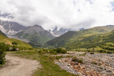 Gürcistan, Svaneti Bölgesi, Ushguli 'deki Büyük Kafkasya Dağları' ndaki Shkhara Buzulu 'na giden bir yürüyüş yolu. Arkada karla kaplı dağlar var. Seyahat tutkusu. Vahşi doğa. Bulutlu ve bulutlu