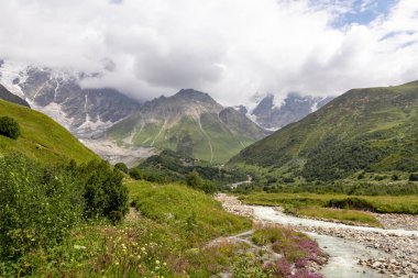 Patara Enguri Nehri Gürcistan 'ın Svaneti Bölgesi, Ushguli' deki Büyük Kafkasya Dağları 'ndaki bir vadiden aşağı akıyor. Shkhara Dağı bulutlarla kaplı. Karla kaplı dağlar. Buzul.