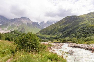 Patara Enguri Nehri Gürcistan 'ın Svaneti Bölgesi, Ushguli' deki Büyük Kafkasya Dağları 'ndaki bir vadiden aşağı akıyor. Shkhara Dağı bulutlarla kaplı. Karla kaplı dağlar. Buzul.