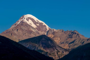 Gürcistan 'ın Büyük Kafkasya Dağları' ndaki Kazbegi Dağı 'nda panoramik bir sabah manzarası. Kar kaplı zirvenin üzerinde açık bir gökyüzü. Khokh menzili. Gün batımı, gün doğumu. Gizemli. Macera ve keşif