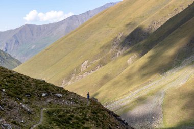 Gürcistan, Kazbegi Bölgesi 'ndeki Büyük Kafkasya Dağları' nda yeşil tepelerde panoramik manzaralı ve dağ zirvelerinin keskin sırtlarında yürüyüş yapan bir kadın. Seyahat tutkusu.