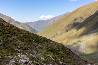 Gürcistan, Kazbegi Bölgesi 'ndeki Büyük Kafkasya Dağları' nda yeşil tepelerde panoramik manzaralı ve dağ zirvelerinin keskin sırtlarında yürüyüş yapan bir kadın. Seyahat tutkusu.