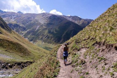 Gürcistan, Kazbegi Bölgesi 'ndeki Büyük Kafkasya Dağları' nda yeşil tepelerde panoramik manzaralı ve dağ zirvelerinin keskin sırtlarında yürüyüş yapan bir kadın. Seyahat tutkusu.
