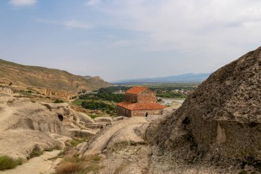 A female tourist enjyoing the view from the ancient cave city of Uplistsikhe overlooking the Mtkvari river in the Shida Kartli Region of Georgia,Caucasus,Eastern Europe.Woman in red dress. Near Gori clipart