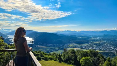 A woman standing at the viewing platform of a chapel at the top of Oswaldiberg with the view on the Lake Ossiach in Austrian Alps, Carinthia. The woman enjoys panoramic view. Morning vibe, Freedom clipart