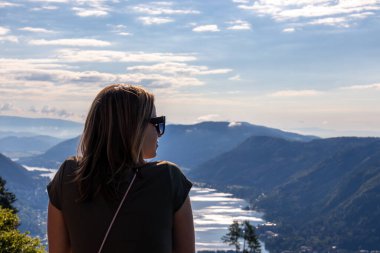 A woman standing at the viewing platform of a chapel at the top of Oswaldiberg with the view on the Lake Ossiach in Austrian Alps, Carinthia. The woman enjoys panoramic view. Morning vibe, Freedom clipart