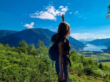 A woman standing at a viewing point near the top of Oswaldiberg with the view on the Lake Ossiach in Austrian Alps, Carinthia. The hiker enjoys a panoramic view on the Ossiacher Tauern. Freedom clipart