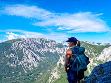 A Woman with a hiking backpack standing on the rock with a view on the Alpine mountain chains in Austria, Hochschwab region in Styria. Freedom and adventure vibes. Oberort, Tragoess clipart