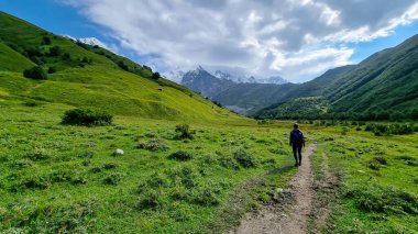 Gürcistan, Svaneti Bölgesi 'ndeki Büyük Kafkasya Dağları' ndaki Tetnuldi, Gistola ve Lakutsia 'nın karlı zirvelerini gören bir vadide yürüyüş yapan bir kadın. Seyahat tutkusu.