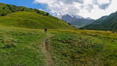 Gürcistan, Svaneti Bölgesi 'ndeki Büyük Kafkasya Dağları' ndaki Tetnuldi, Gistola ve Lakutsia 'nın karlı zirvelerini gören bir vadide yürüyüş yapan bir kadın. Seyahat tutkusu.