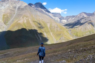 Gürcistan, Kazbegi Bölgesi 'ndeki Büyük Kafkasya Dağları' ndaki Chaukhi Geçidi 'ni oluşturan Chaukhi tepelerini izleyen bir kadın. Dişi sırt çantası sakinliğin tadını çıkarıyor. Koşun!