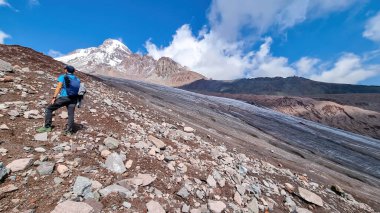 Gürcistan, Kafkasya 'daki Kazbeg Dağı manzaralı Gergeti Buzulu eteğinde duran bir adam. Kar kaplı tepenin altında çorak yamaçlar. Keskin tepenin etrafında çok az bulut toplanıyor. Huzur