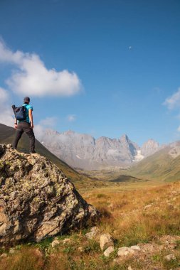 Gürcistan, Kazbegi Bölgesi 'ndeki Büyük Kafkasya Dağları' ndaki Chaukhi topluluğunun keskin dağ zirvelerini izleyen bir adam. Yürüyüşçü büyük bir kayanın üzerinde duruyor. Gürcü Dolomitler. Özgürlük