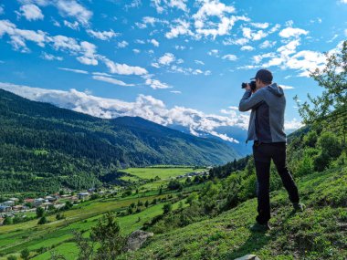 Erkek bir fotoğrafçı, Gürcistan 'ın Yukarı Svaneti bölgesindeki Büyük Kafkasya Dağları' ndaki Mestia vadisinde inanılmaz manzaranın keyfini çıkarıyor. Bulutlar karlı dağ zirvelerini kaplıyor. Açık havada.