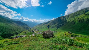 Georgia, Svaneti Bölgesi 'ndeki Büyük Kafkasya Dağları' ndaki Shkhara Buzulu 'nun yakınındaki Ushguli köyünde hava manzaralı bir kayanın üzerinde duran bir adam. Chubedishi bakış açısı. Patara Enguri Nehri.