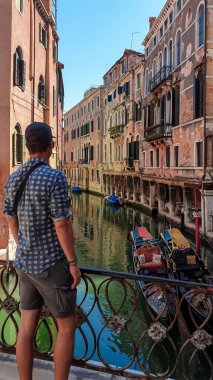 Venedik, Veneto, İtalya ve Avrupa 'daki su kanallarına bakan eski köprüde duran adam. Venedik mimari simgeleri ve kanal boyunca uzanan eski evler. Yaz aylarında şehir turizmi