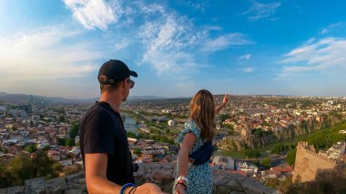 Panoramik şehir manzarası, Mtkvari nehri üzerindeki Barış Köprüsü, Tiflis Sameda Katedrali ve Tiflis, Gürcistan, Kafkasya 'daki Başkanlık Sarayı' nın keyfini çıkaran bir çift. Turizm. Seyahat güzergahı. Şehir gezisi.