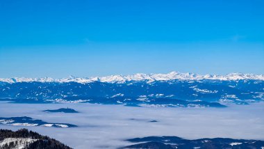 Avusturya 'nın Carinthia kentindeki Karawanks dağlarının karla kaplı tepelerinde Hochobir' den panoramik manzara. Julian Alps. Avusturya Alpleri, Avrupa 'da kış harikalar diyarı. Vadi bulutlarla kaplı. Yüksek Tauern Alpleri