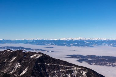 Avusturya 'nın Carinthia kentindeki Karawanks dağlarının karla kaplı tepelerinde Hochobir' den panoramik manzara. Julian Alps. Avusturya Alpleri, Avrupa 'da kış harikalar diyarı. Vadi bulutlarla kaplı. Yüksek Tauern Alpleri