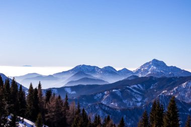 Avusturya, Carinthia 'daki Karawanks dağlarının karla kaplı tepelerinde panoramik manzara. Julian Alps. Avusturya Alpleri, Avrupa 'da kış harikalar diyarı. Kayak turu, kar ayakkabısı yürüyüşü. Hochobir. Mavi sisli tepeler.