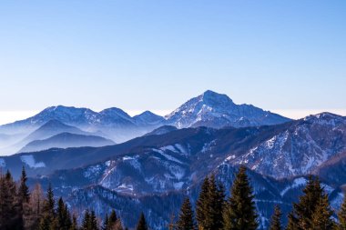 Avusturya, Carinthia 'daki Karawanks dağlarının karla kaplı tepelerinde panoramik manzara. Julian Alps. Avusturya Alpleri, Avrupa 'da kış harikalar diyarı. Kayak turu, kar ayakkabısı yürüyüşü. Hochobir. Mavi sisli tepeler.