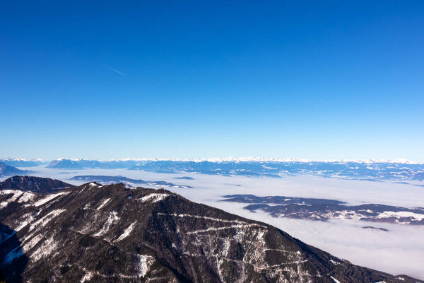 Panoramic view from Hochobir on snow capped mountain peaks of Karawanks in Carinthia, Austria. Julian Alps. Winter wonderland in the Austrian Alps, Europe. Valley covered with clouds. High Tauern Alps
