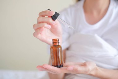 Asyalı kadın yatakta oturuyor ve El 'e serum uyguluyor..