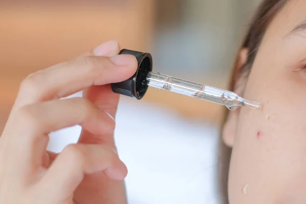 stock image Asia woman sitting on bed and applying serum on face.