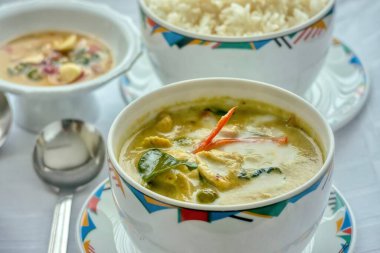 Tayland usulü yeşil köri tavuğu ve pirinçle servis edilen beyaz masa örtüsü üzerindeki batı stil kaseleri. Sığ alan derinliği.