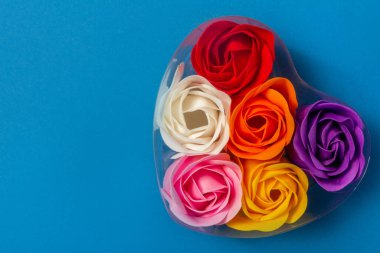 Kadınlar için güzel bir hatıra: çok renkli pembe güller mavi arka planda kalp şeklinde bir kutuda fotokopi alanı, üst manzara. Aşk konsepti, cilt bakımı, güzellik, Sevgililer Günü.