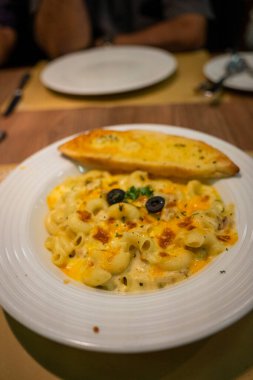 Beyaz tabakta sarımsaklı ekmekle peynirli makarna resmi.