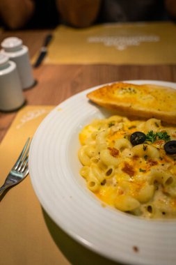 Beyaz tabakta sarımsaklı ekmekle peynirli makarna resmi.