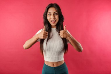 Neşeli kahverengi saçlı kadın kırmızı arka planda izole edilmiş kırbaç takıyor. Elleriyle olumlu jest yapıyor. Gülümsüyor ve mutlu..