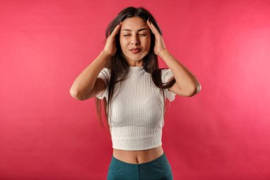 Kahverengi saçlı, beyaz kurdeleli bir kadın kırmızı arka planda izole edilmiş, genç ve güzel bir kız, şakaklarda el ele tutuşuyor, baş ağrısı çekiyor..