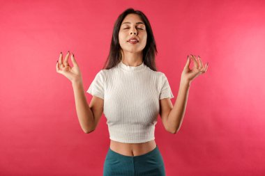 Güzel esmer kadın, kırmızı arka planda izole edilmiş gözleri kapalı, parmaklarını Mudra jestinde tutuyor. Meditasyon, din ve ruhani uygulamalar. Huzur ve sakinlik. Tüm gerginliği ve stresi boşaltır..