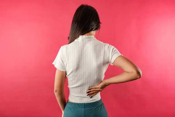 Young beautiful woman wearing ribbed crop isolated over red background Spinal cord problems, suffering from pain in back. Medical concept. Showing pain.
