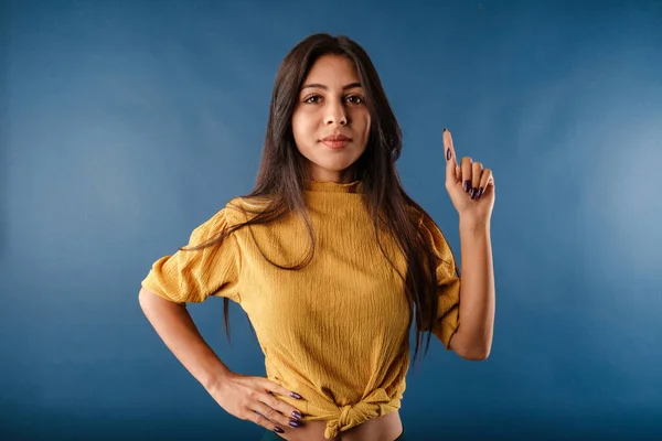 Beautiful brunette woman wearing isolated over blue background shaking index finger and grimacing hesitant, have suggestion or worry, saying her opinion, judging awkward situation.