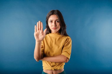 Portrait of cheerful woman isolated over blue background showing with palm hand stop sign gesture. No pass. Now put a stop to this! Warning expression with negative and serious gesture on the face.