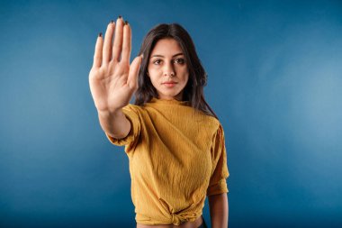 Portrait of cute dark-haired woman wearing casual top isolated over blue background doing stop sing with palm of the hand. Warning expression with negative and serious gesture on the face.