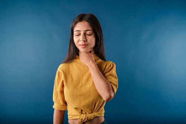 Woman isolated over blue background holding her inflamed throat. Medical concept, Sore throat. Having sore throat, holding hand on her neck, suffering from throat pain, painful swallowing.