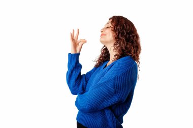 Side view of cute millennial woman wearing pullover sweater standing isolated over white background closed eyes arm fingers show gourmet gesture. Pouted lips. Trying yummy dessert.