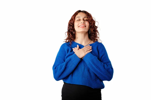Young woman smiling confident standing isolated over white background hold hands on heart chest feel grateful and thankful. Show gratitude, love and care, pray or visualize. Religion, faith concept.