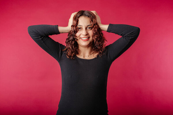 Portrait of cheerful woman wearing black ribbed dress standing isolated over red background emotional surprised woman holding hands by the head and looking at camera. Very happy and cannot believe it.