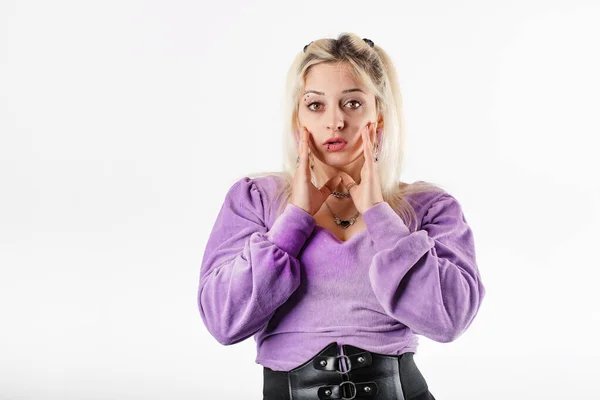 Blonde millennial woman wearing ribbed blouse standing isolated over white background looking excited holding her mouth opened, hands on head. Can't believe what hear.