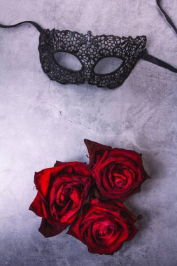 Dantelden yapılmış siyah maske ve gri arka planda üç gül.
