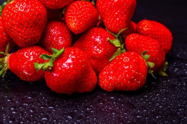 Siyah zemin üzerinde su damlaları olan birkaç çilek.