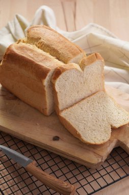 Yeni pişmiş bir somun beyaz buğday ekmeği ve tahta üzerinde dilimler.